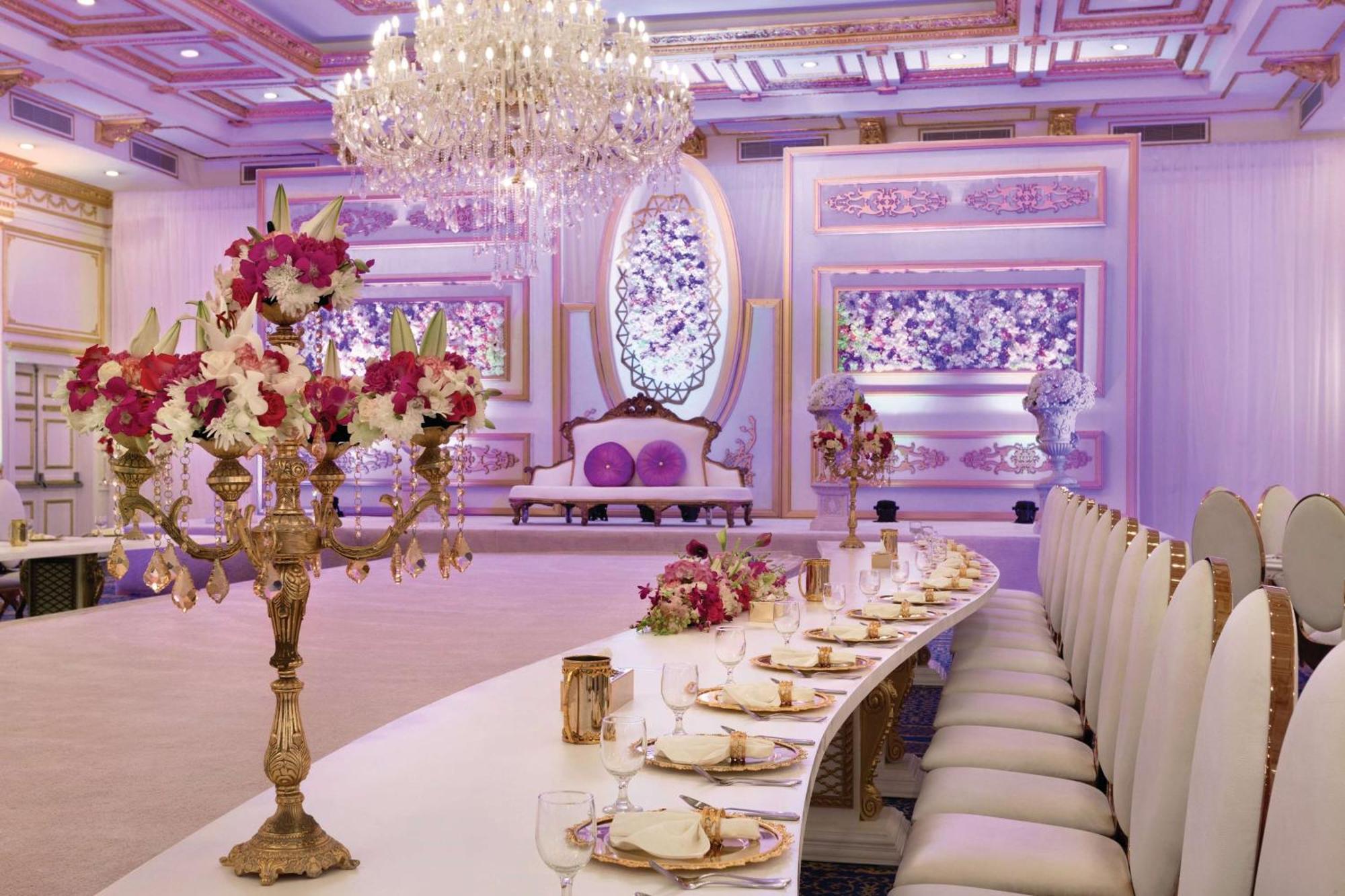 Grand Regency Doha, Trademark Collection By Wyndham Exterior foto The photo displays an elegantly decorated banquet or dining hall. It features a long, curved table set for a formal event, with fine china and floral centerpieces. Luxurious decorations include a grand chandelier hanging from the ceiling, and the wal