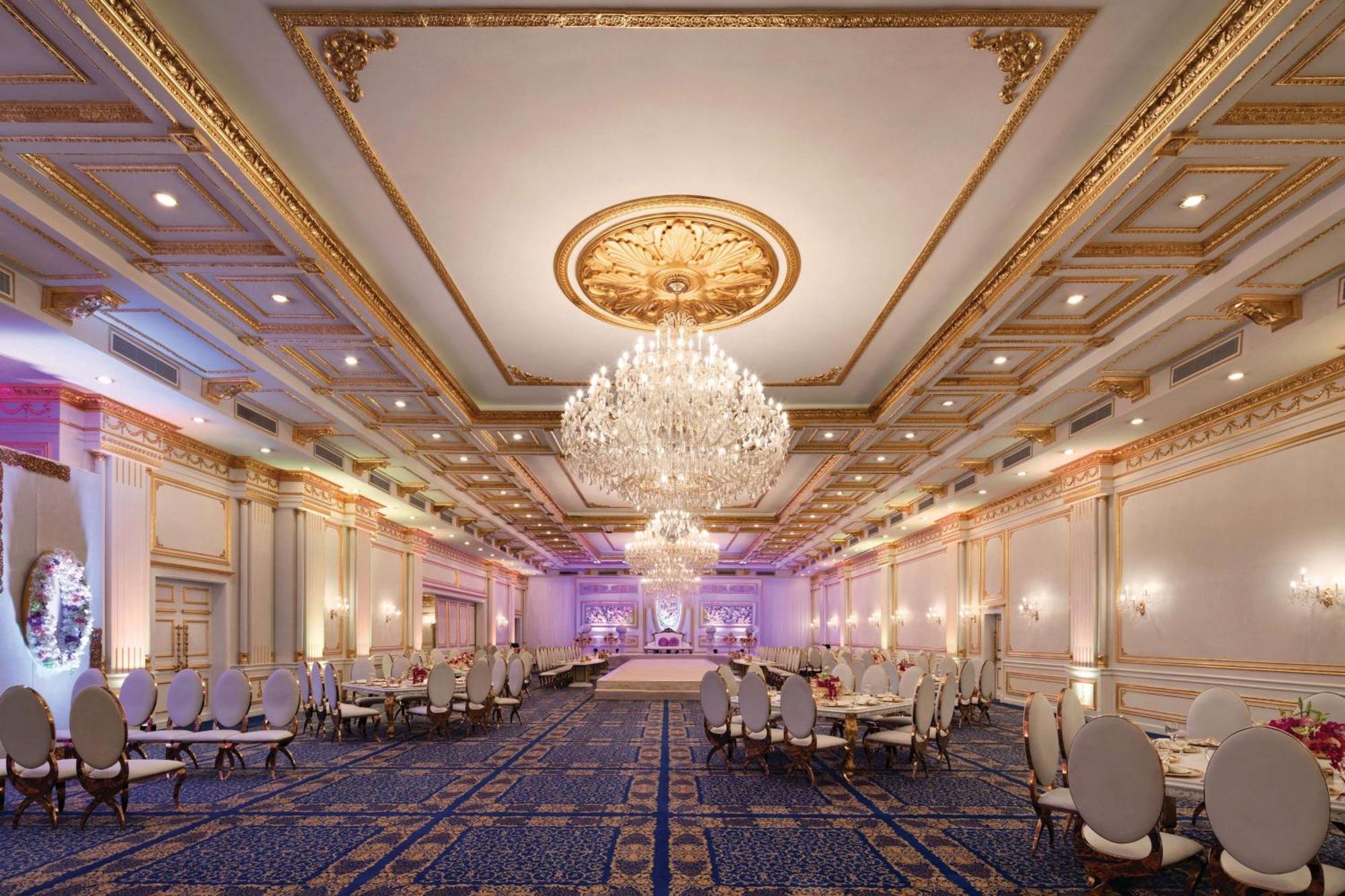 Grand Regency Doha, Trademark Collection By Wyndham Exterior foto The photo shows an elegant banquet hall with luxurious decor. The room features high ceilings adorned with intricate gold details and a large chandelier that hangs in the center, providing soft illumination. There are several round tables with plush 