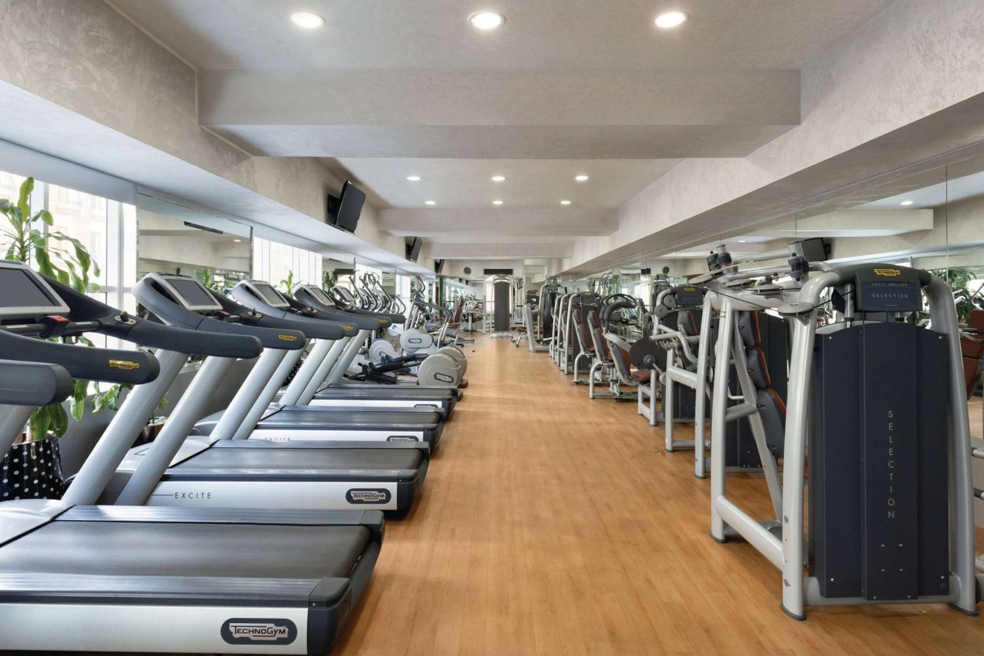 Grand Regency Doha, Trademark Collection By Wyndham Exterior foto The photo shows the interior of a gym or fitness center. It features a row of modern treadmills lined up against a wall, with a polished wooden floor. The space is brightly lit with recessed ceiling lights, and there are large mirrors on the walls, e
