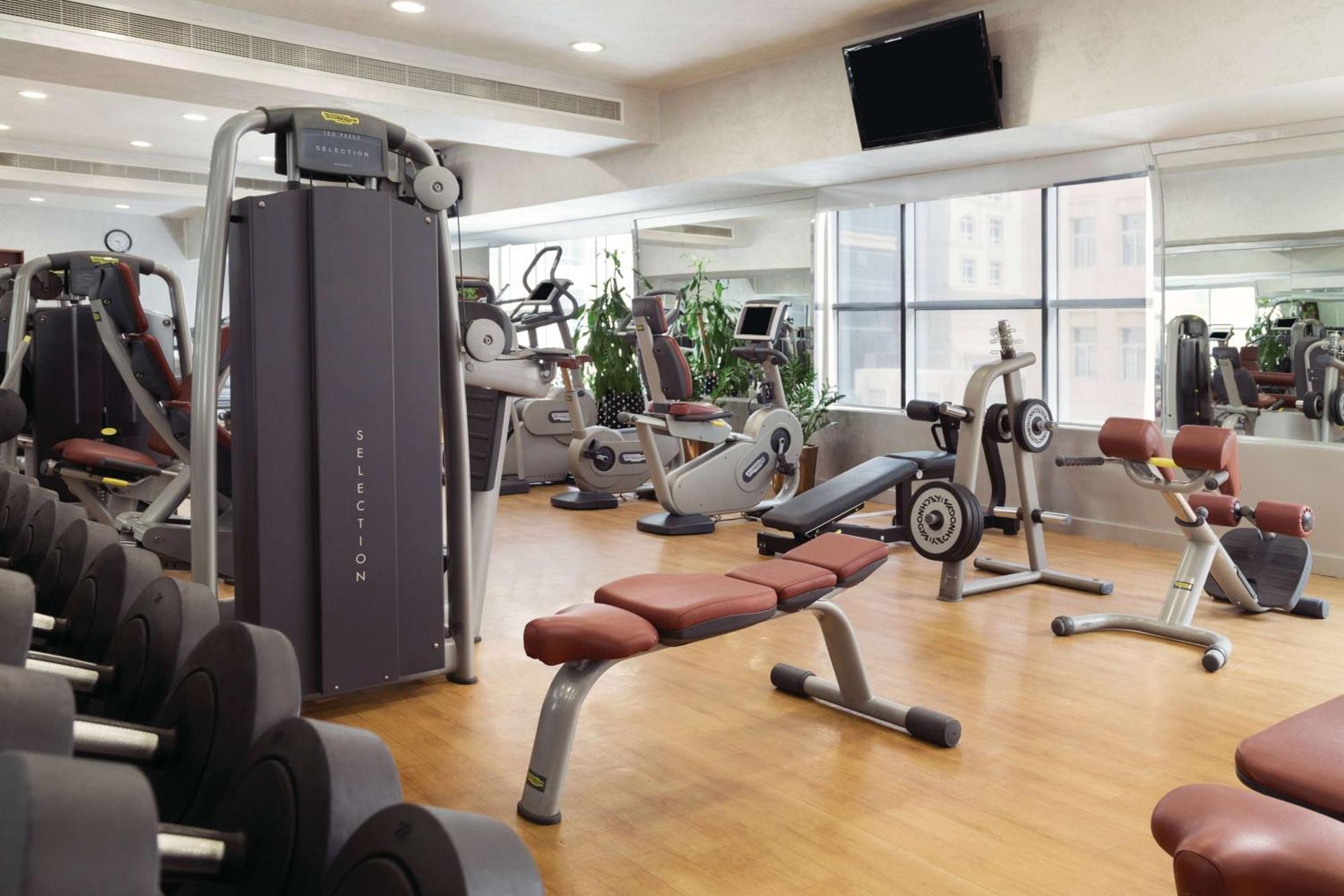 Grand Regency Doha, Trademark Collection By Wyndham Exterior foto The photo shows a fitness gym with various exercise equipment. There are weight machines, benches, and cardio machines such as stationary bikes and treadmills. The space has large windows allowing natural light to enter, and there are mirrors on the 