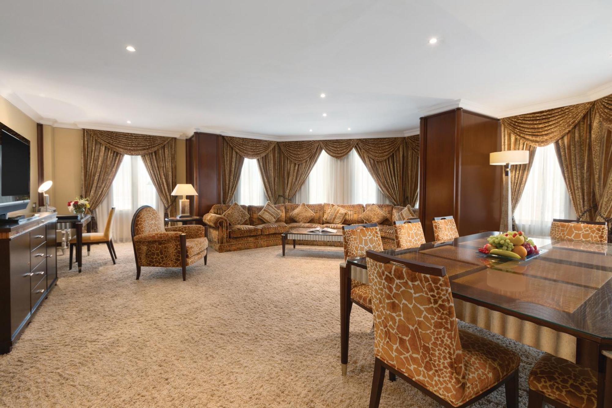 Grand Regency Doha, Trademark Collection By Wyndham Exterior foto The photo shows a spacious and elegantly designed living area. There are large windows dressed with luxurious curtains, allowing natural light to fill the room. The seating arrangement features a comfortable sofa with various cushions and several sty